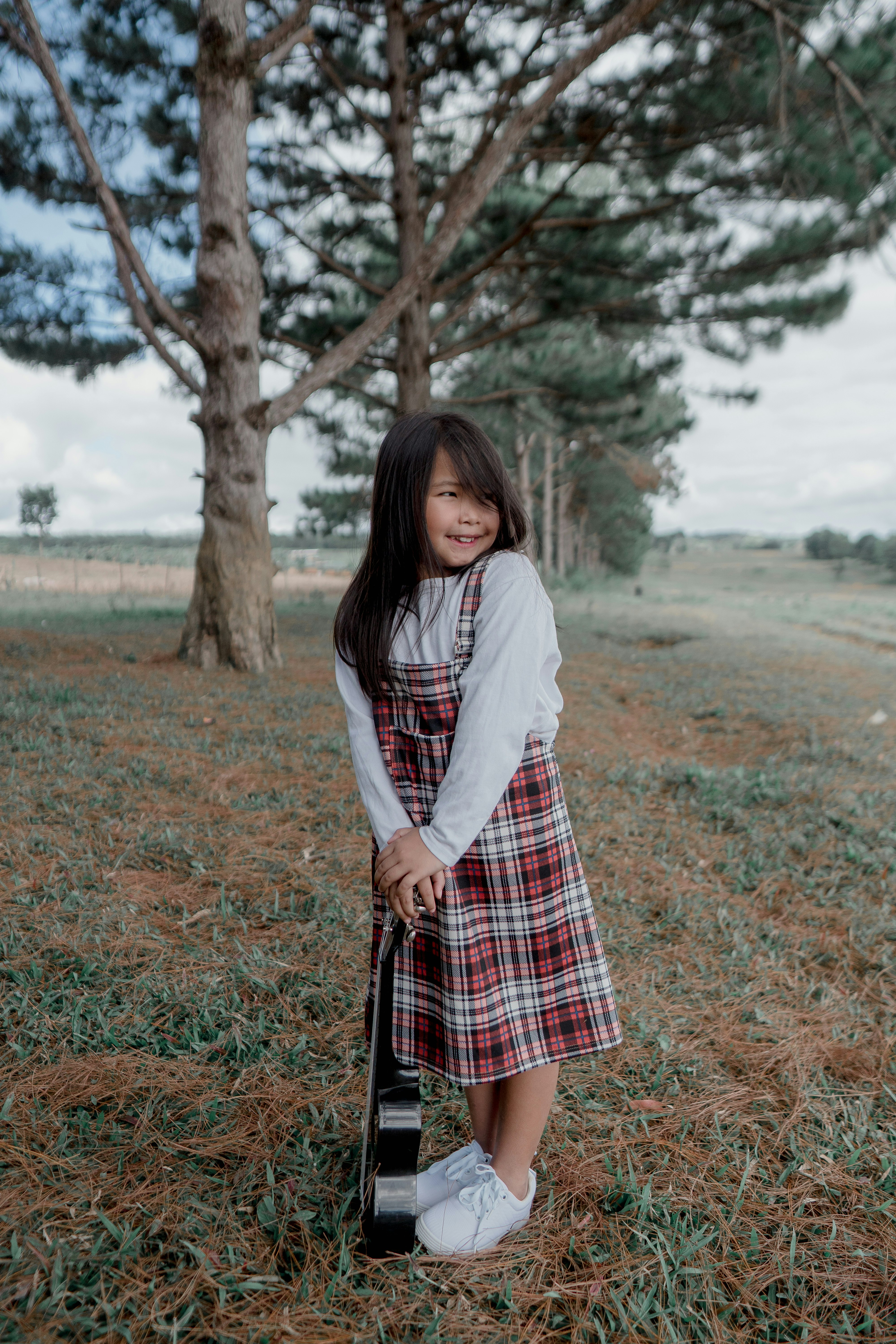 woman in white long sleeve shirt and red and black plaid skirt standing on green grass